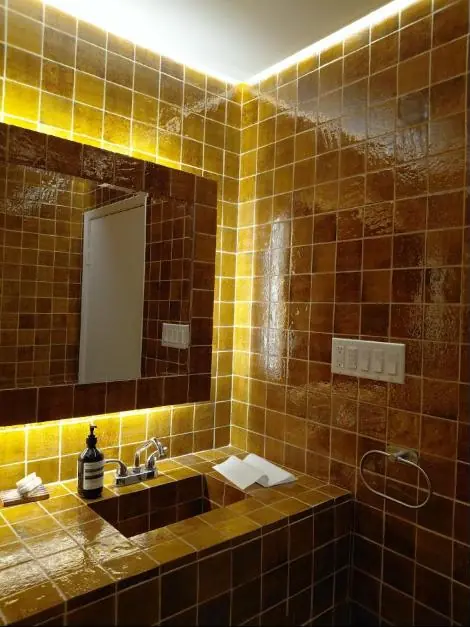The washroom tiled floor to ceiling in glossy amber with a glowing mirror
