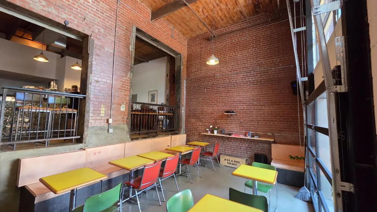 The brick hall with banquettes, yellow tables and the open garage door