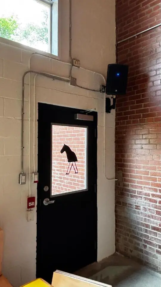 A black door with the Vers horse in the window, next to the brick wall