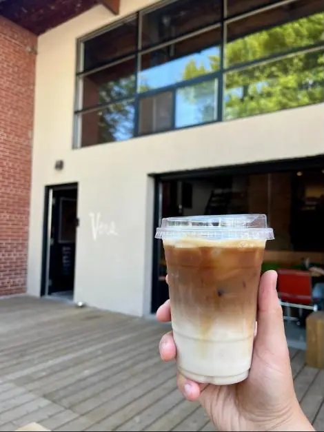 An iced latte held up in front of the Vers storefront